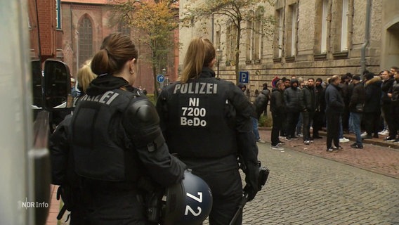 Polizistinnen beobachten eine Gruppe von Menschen vor einem Gebäude. © Screenshot 