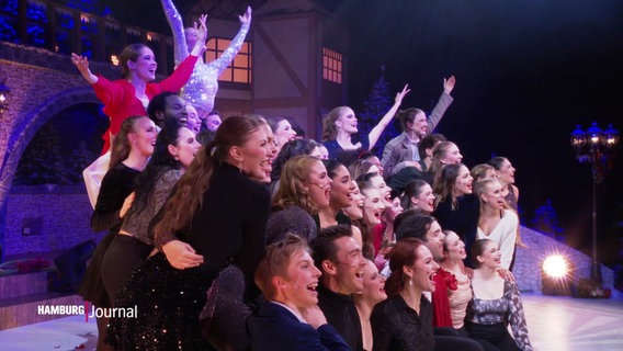 Szene einer Musicalaufführung, einige Künstler und Künstlerinnen stehen im Pulk auf der Bühne und singen. © Screenshot 