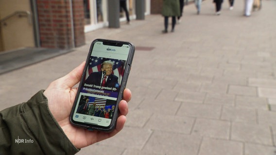 Eine Person hat einen Nachrichtenbeitrag auf dem Handy geöffnet, der Donald Trump als Sieger der US-Präsidentschaftswahlen 2024 zeigt. © Screenshot 