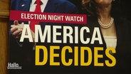 Plakat mit Fotos von Donald Trump und Kamala Harris, darüber die Überschrift: "Election night watch - America decides". © Screenshot 