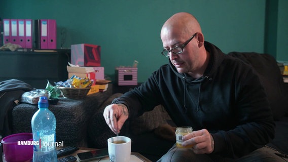 Der ehemals obdachlose Dave sitzt in seiner über das Projekt "Housing First" vermittelten Wohnung und trinkt einen Tee. © Screenshot 