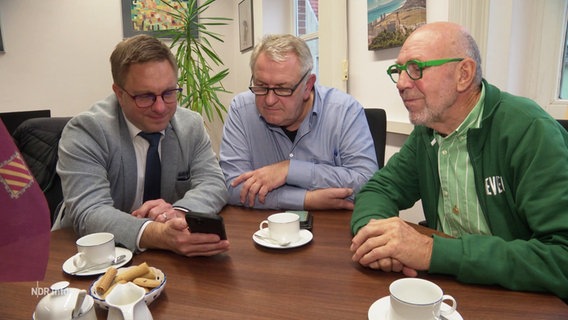 Der Jever' Bürgermeister und zwei weitere Männer aus Jever sitzen an einem Tisch und Facetimen mit einem Bekannten aus der spanischen Partnerstadt Cullera. © Screenshot 