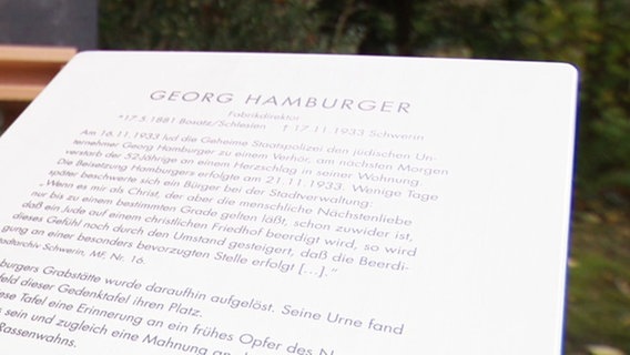 Eine Gedenktafel auf dem alten Friedhof Schwerin steht vor einer Staffelei die das Porträt von Georg Hamburger zeigt. © Screenshot 