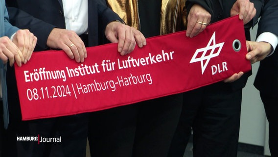 Mehrere Personen halten ein Banner mit der Aufschrift "Eröffnung Institut für Luftverkehr". © Screenshot 