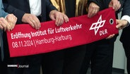 Mehrere Personen halten ein Banner mit der Aufschrift "Eröffnung Institut für Luftverkehr". © Screenshot 