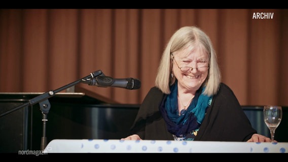 Autorin Helga Schubert sitzt vor einem Mikro, auf einer Bühne und lacht (Archivbild). © Screenshot 