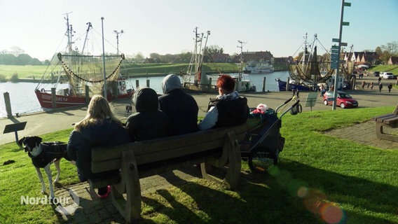 Touristen in Greetsiel sitzen auf einer Bank am Hafen. © Screenshot 