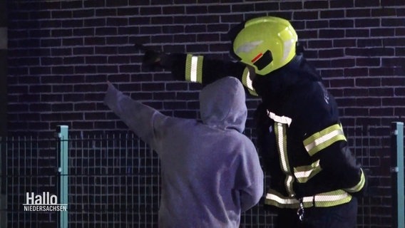 Ein Junge mit lila Pulli zeigt einer Feuerwehrperson mit Uniform und Helm den Weg. © Screenshot 