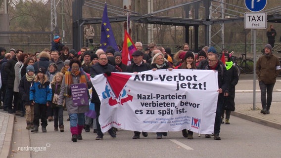 Demonstranten laufen auf der Straße und halten ein Banner hoch. © Screenshot 