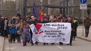 Demonstranten laufen auf der Straße und halten ein Banner hoch. © Screenshot 