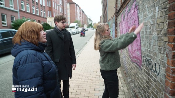 Drei Menschen vor einer Wand an einer Straße. © Screenshot 