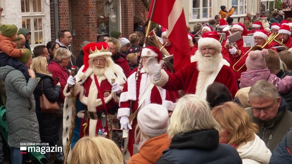 Viele Weihnachtsmänner laufen bei einem Umzug mit dänischer Fahne durch eine Menschenmenge. © Screenshot 