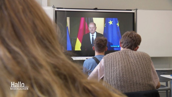 Schülerinnen und Schüler von hinten zu sehen, die auf einen Fernseher schauen. Übertragen wird die Rede von Olaf Scholz zur Auflösung der Ampel-Koalition. © Screenshot 