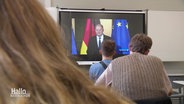 Schülerinnen und Schüler von hinten zu sehen, die auf einen Fernseher schauen. Übertragen wird die Rede von Olaf Scholz zur Auflösung der Ampel-Koalition. © Screenshot 