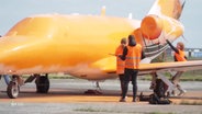 Mehrere Aktivistinnen und Aktivisten der "Letzten Generation" besprühen einen Privatjet mit orangener Farbe. © Screenshot 