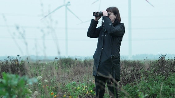 Stefanie Neumann steht auf einem Feld und blick durch ein Fernglas. © Screenshot 