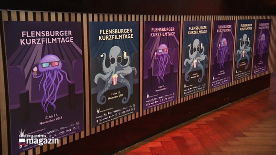 An einer Wand hängen mehrere Plakate der Flensburger Kurzfilmtage. Sie zeigen Illustrationen von einer Qualle und einem Oktopus, die mit Popcorn in einem Kinosaal sitzen. © Screenshot 