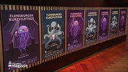 An einer Wand hängen mehrere Plakate der Flensburger Kurzfilmtage. Sie zeigen Illustrationen von einer Qualle und einem Oktopus, die mit Popcorn in einem Kinosaal sitzen. © Screenshot 