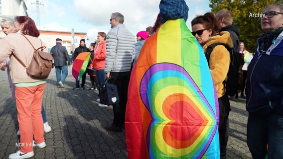 Eine Frau steht in eine Regenbogenflagge gehüllt vor dem Rathaus von Neubrandenburg. © Screenshot 