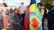 Eine Frau steht in eine Regenbogenflagge gehüllt vor dem Rathaus von Neubrandenburg. © Screenshot 