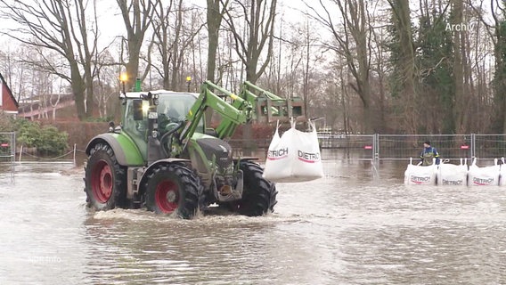 Ein Bagger hält einen Sandsack und fährt durch das Hochwasser (Archivbild). © Screenshot 