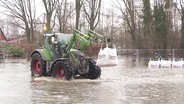 Ein Bagger hält einen Sandsack und fährt durch das Hochwasser (Archivbild). © Screenshot 