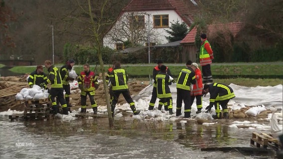 Mehrere Einsatzkräfte der Feuerwehr versuchen bei Hochwasser einen provisorischen Staudamm mit Sandsäcken zu errichten. © Screenshot 