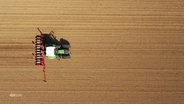 Blick aus der Vogelperspektive: Ein Traktor fährt über ein Feld und verteilt Düngemittel. © Screenshot 