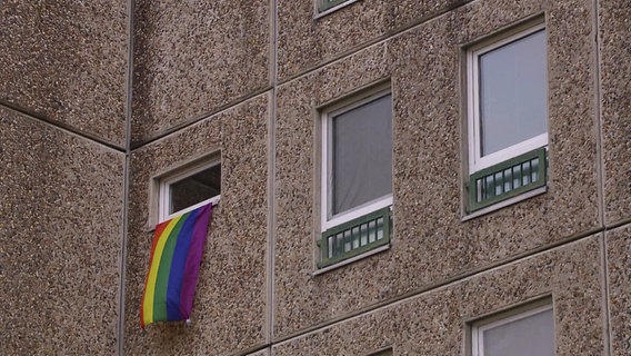 An einer Waschbeton-Fassade hängt eine Regenbogen-Flagge aus einem Fenster. © Screenshot 