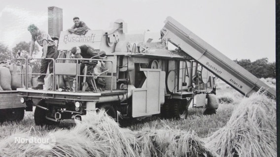 Ein historisches Schwarz-Weiß-Foto zeigt Feldarbeiter auf einer größeren Dieselmaschine für die landwirtschaftliche Arbeit. © Screenshot 