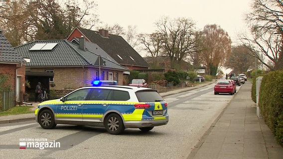 Ein Polizeiauto steht mit eingeschaltetem Blaulicht queer auf einer Straße vor einem Wohnhaus. © Screenshot 