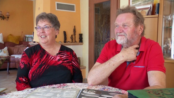 Eine Frau und ein Mann sitzen am Wohnzimmertisch vor einem Fotoalbum. © Screenshot 