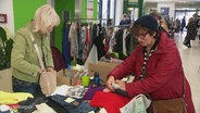 Auf einem Indoor-Flohmarkt schließen zwei Frauen an einem Stand einen Kauf ab. © Screenshot 