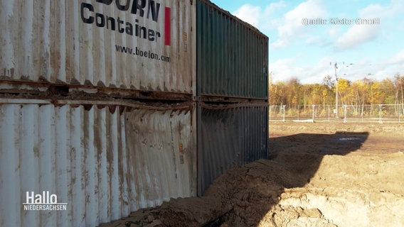 Zerbeulte Container und ein Krater im Sand sind nach einer kontrollierten Sprengung von zwei Weltkriegsbomben geblieben. © Screenshot 