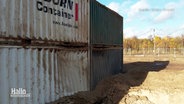 Zerbeulte Container und ein Krater im Sand sind nach einer kontrollierten Sprengung von zwei Weltkriegsbomben geblieben. © Screenshot 