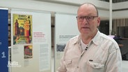 Ralf Hermes, Regionalsprecher Hannover des Reichsbanner Schwarz-Rot-Gold, steht vor den im Landtag ausgestellten Plakaten zum 100-jährigen Jubiläum des Reichsbanners. © Screenshot 