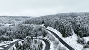 Verschneite Tannen und eine sich einen Hügel entlangwindende Straße im Harz. © Screenshot 