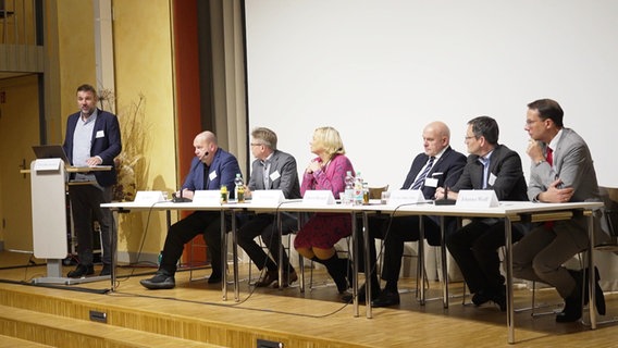 Mehrere Menschen sitzen auf einem Podium. © Screenshot 