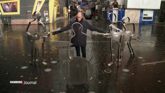 Ein Mann steht inmitten eines Beatles-Denkmals auf der Hamburger Reeperbahn. © Screenshot 