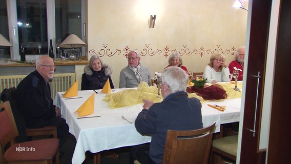 Ältere Frauen und Männer sitzten um einen weiß eingedeckten Tisch. © Screenshot 