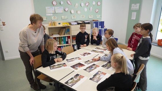 Eine Gruppe Kinder umringt einen Tisch, auf dem Bilder von Schulhofgestaltungen liegen. © Screenshot 