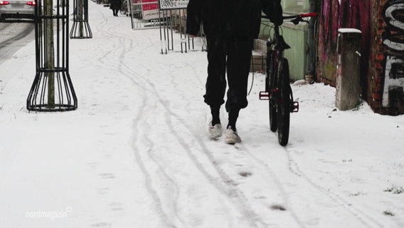 Eine Person schiebt ein Fahrrad über einen verschneiten Gehweg. © Screenshot 