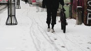 Eine Person schiebt ein Fahrrad über einen verschneiten Gehweg. © Screenshot 