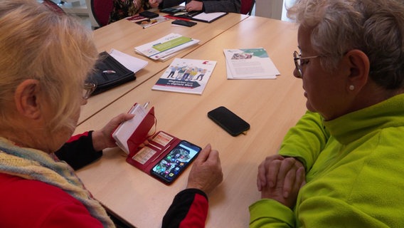 Zwei Frauen sitzen über ein Smartphone gebeugt an einem Tisch. © Screenshot 