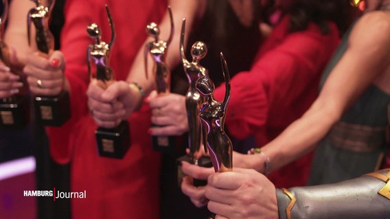 Frauen halten goldene Trophäen in den Händen. © Screenshot 