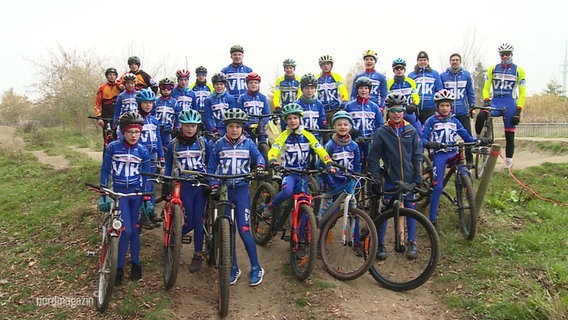 Viele Kinder stehen in Radsport-Kleidung mit ihren Rädern auf der Strecke für ein Gruppenfoto zusammen. © Screenshot 