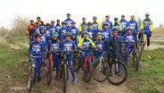 Viele Kinder stehen in Radsport-Kleidung mit ihren Rädern auf der Strecke für ein Gruppenfoto zusammen. © Screenshot 