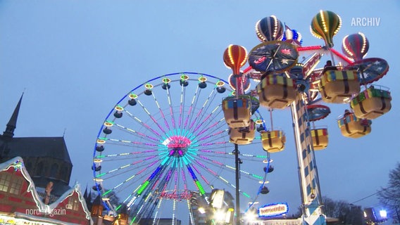 Auf einem Weihnachtsmarkt sind viele bunte Fahrgeschäfte aufgebaut. © Screenshot 