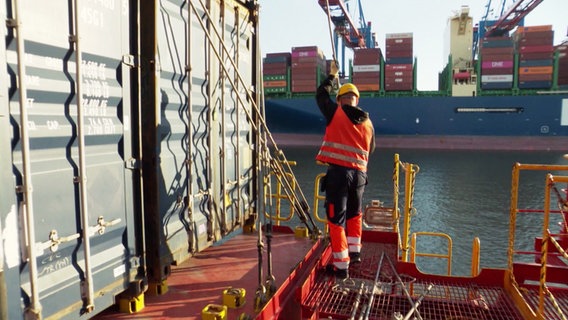 Ein Hafenarbeiter bei der Arbeit auf einem Containerschiff. © Screenshot 