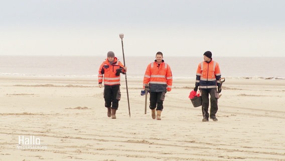 Drei Männer laufen mit technischen Geräten am Strand entlang. © Screenshot 